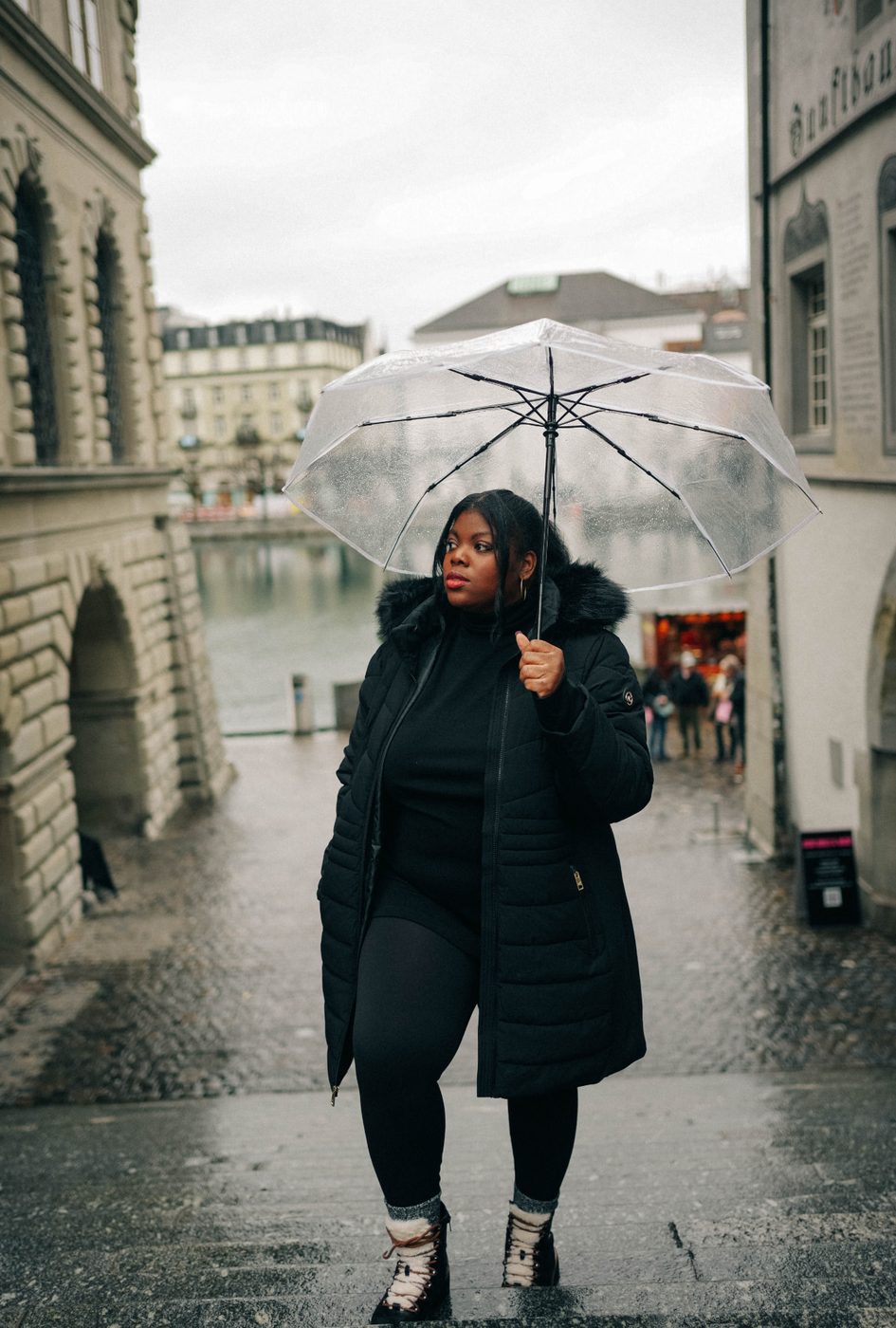 Britt holding a clear umbrella on a rainy cobblestone street in Europe