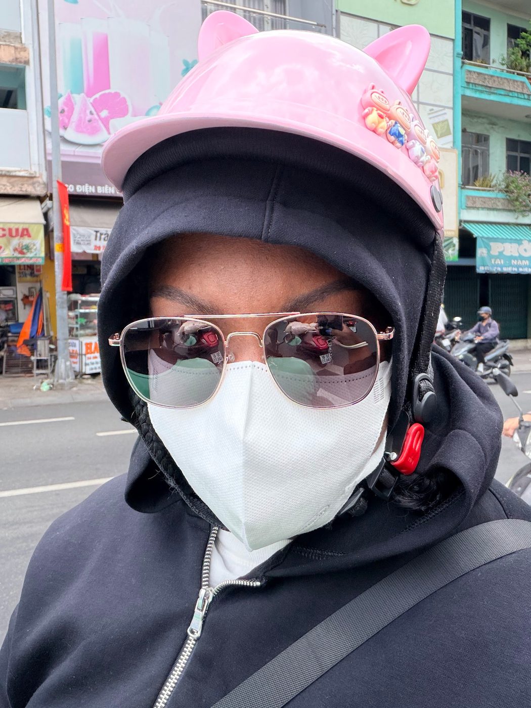 Britt in a pink scooter helmet and sunglasses on a busy street abroad